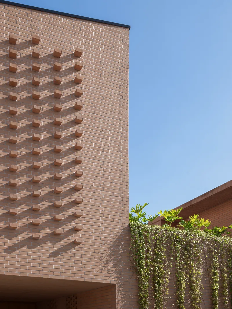 Brick tower with protruding brick pattern beside a planted screen under clear blue sky