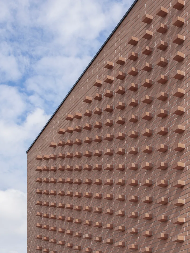Angled view of brick facade with grid of protruding brick elements against scattered clouds