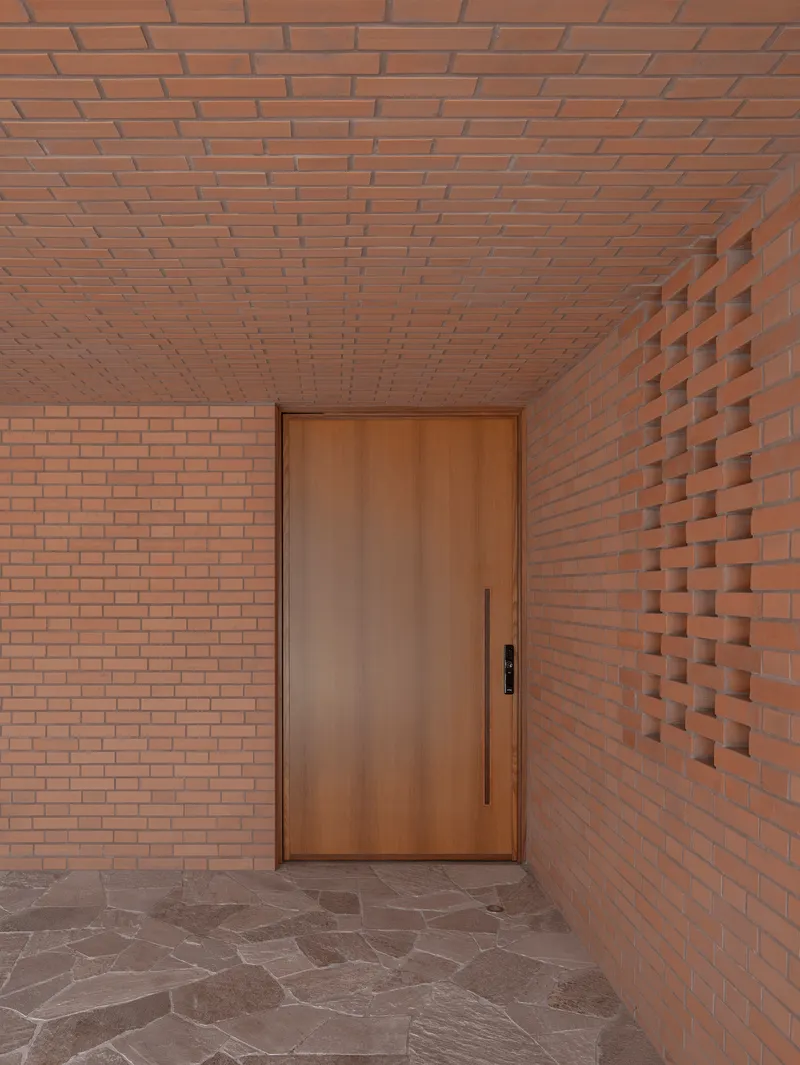 Entry vestibule with timber door flanked by flat and textured brick walls under brick ceiling