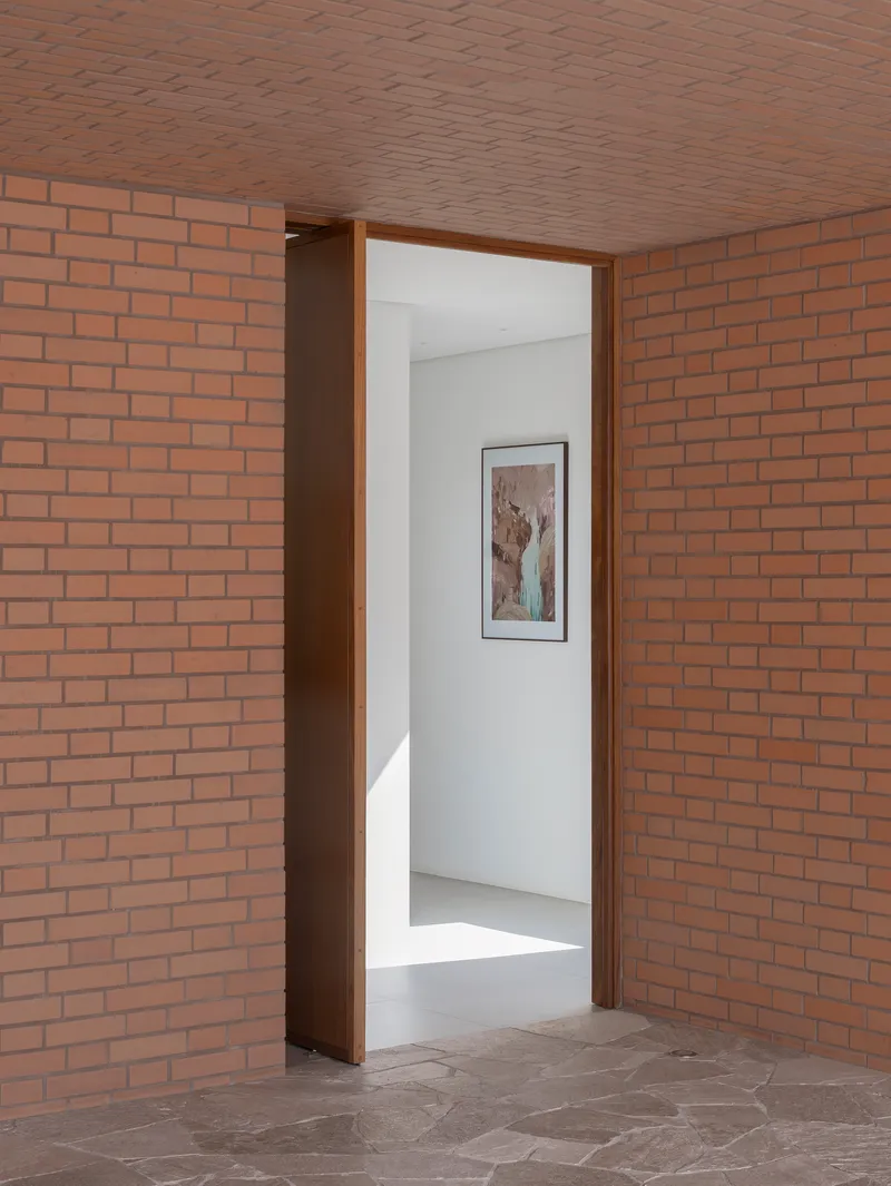 Brick corridor leading through a doorway to a white gallery space with artwork on the wall