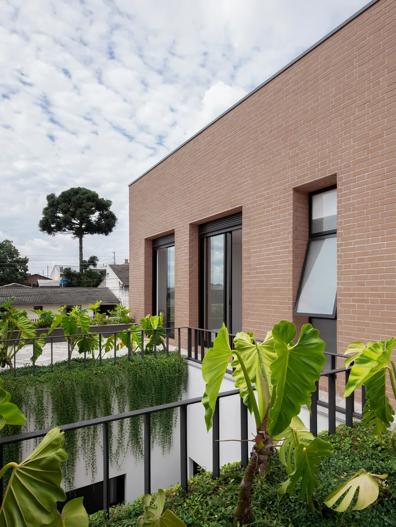 Tan brick facade with planted terrace featuring cascading vines and tropical foliage under cloudy skies