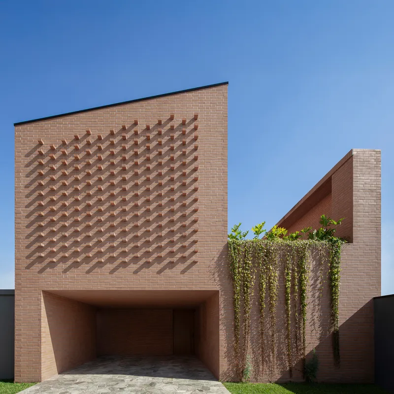 Street facade with protruding brick chevron pattern above a recessed garage and cascading vines at the corner