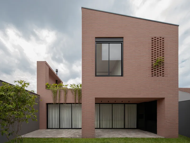 Two-storey brick elevation with staggered window openings and perforated brick ventilation panel under cloudy sky