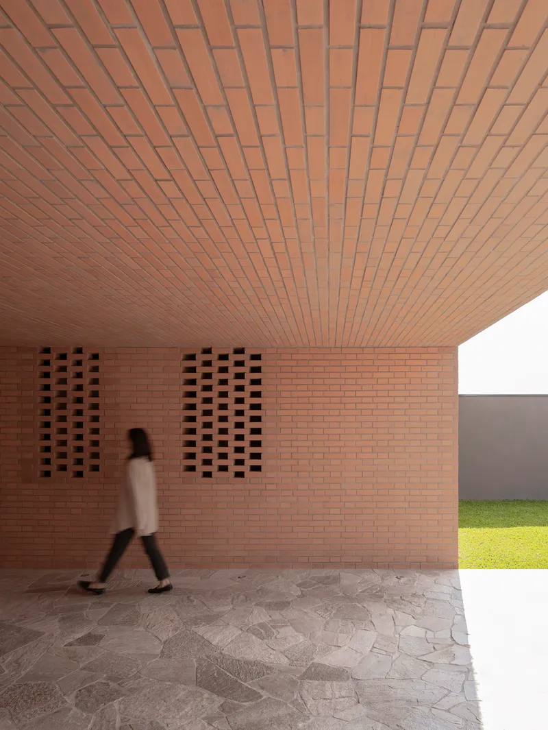 Covered entry passage with brick ceiling and perforated wall panels as a figure walks through