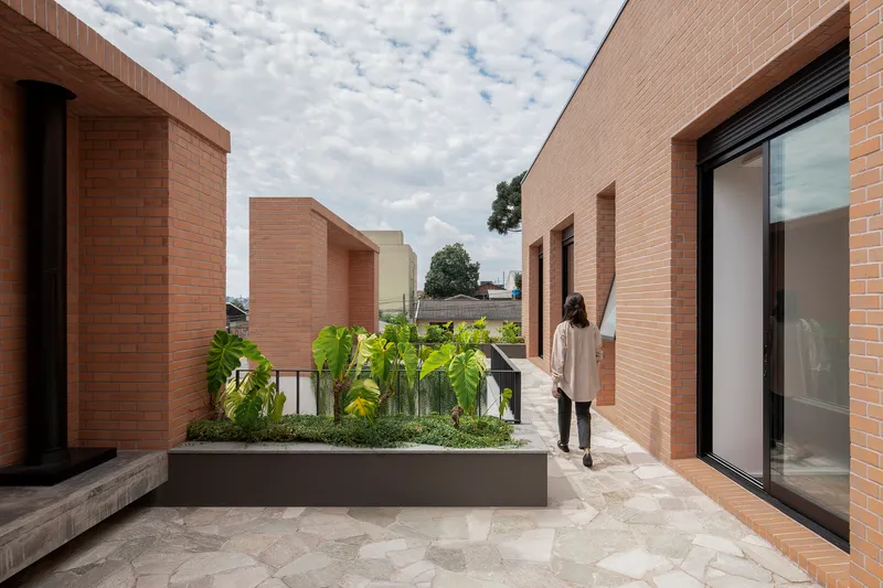 Rooftop terrace with raised planting beds and brick volumes framing views under a cloudy sky