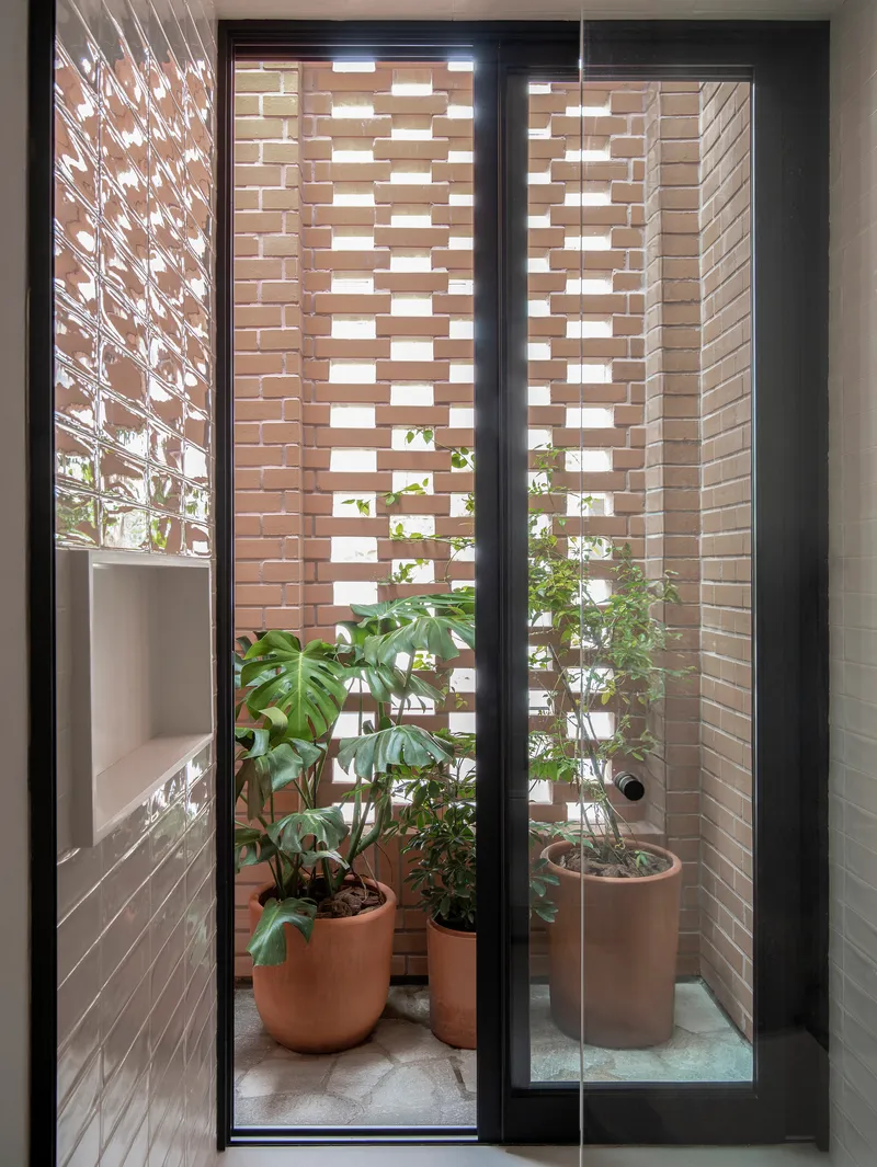 Interior view through glass door to narrow courtyard with perforated brick screen and potted plants