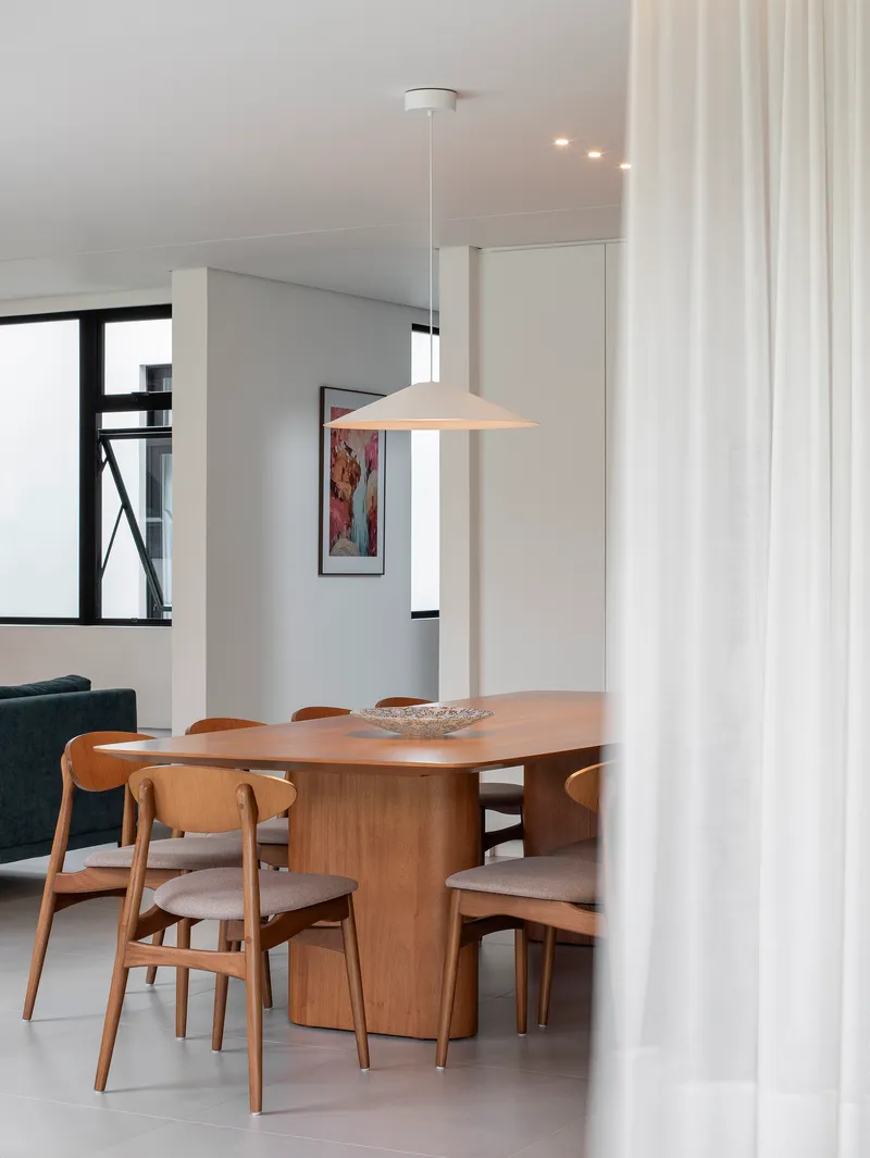 Dining area with timber table and pendant light viewed through a white curtain