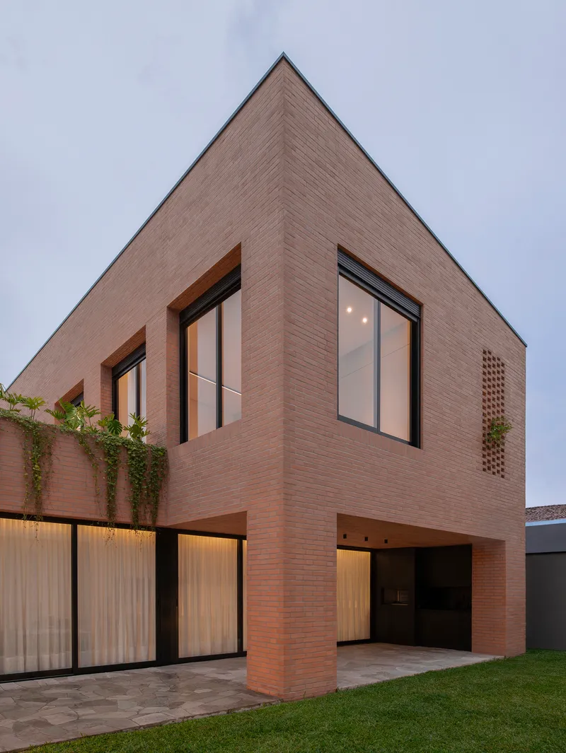 Gabled brick facade with large windows and rooftop planters at twilight