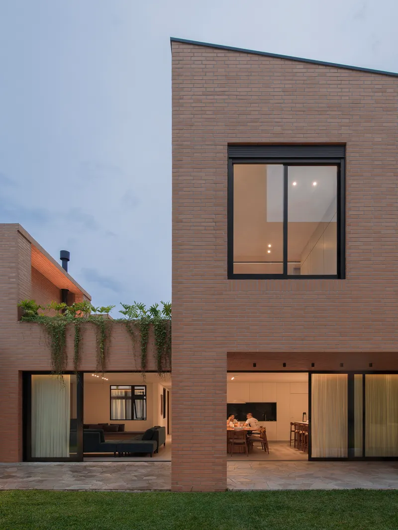 Two-story brick residence with glazed openings and courtyard at dusk