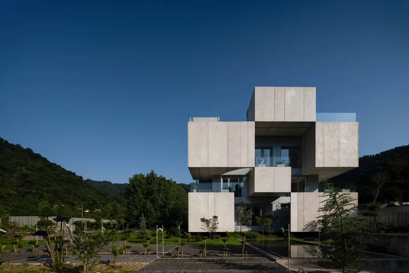 Stacked concrete volumes with cantilevered terraces overlooking a landscaped garden and forested hillside