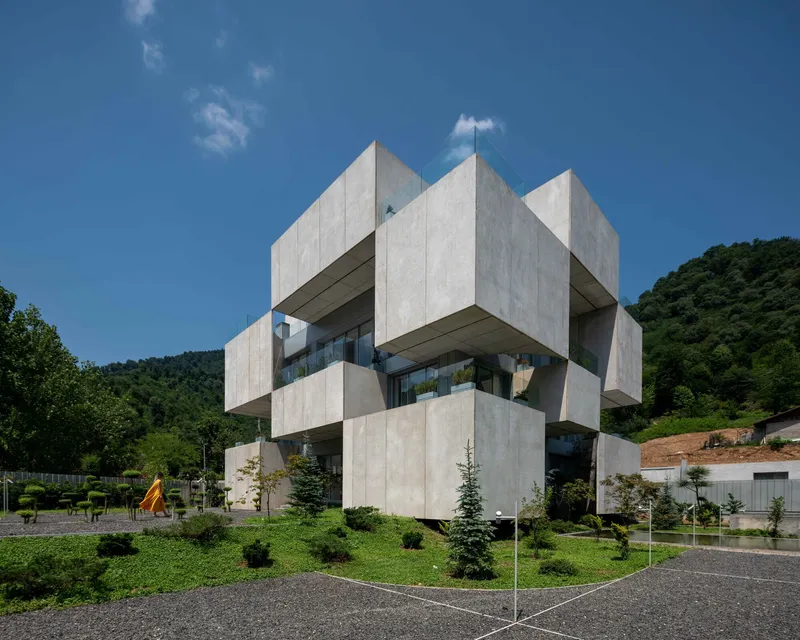 Corner view of the concrete facade showing interlocking cubic forms with recessed glazing under blue sky