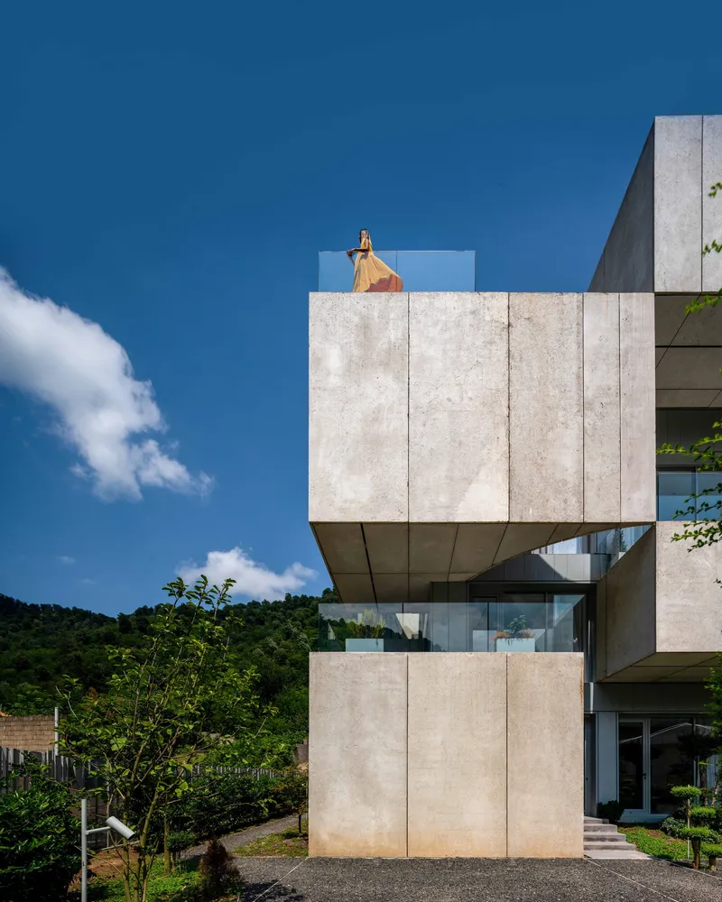 Cantilevered concrete balcony with a figure in orange standing at the upper terrace railing