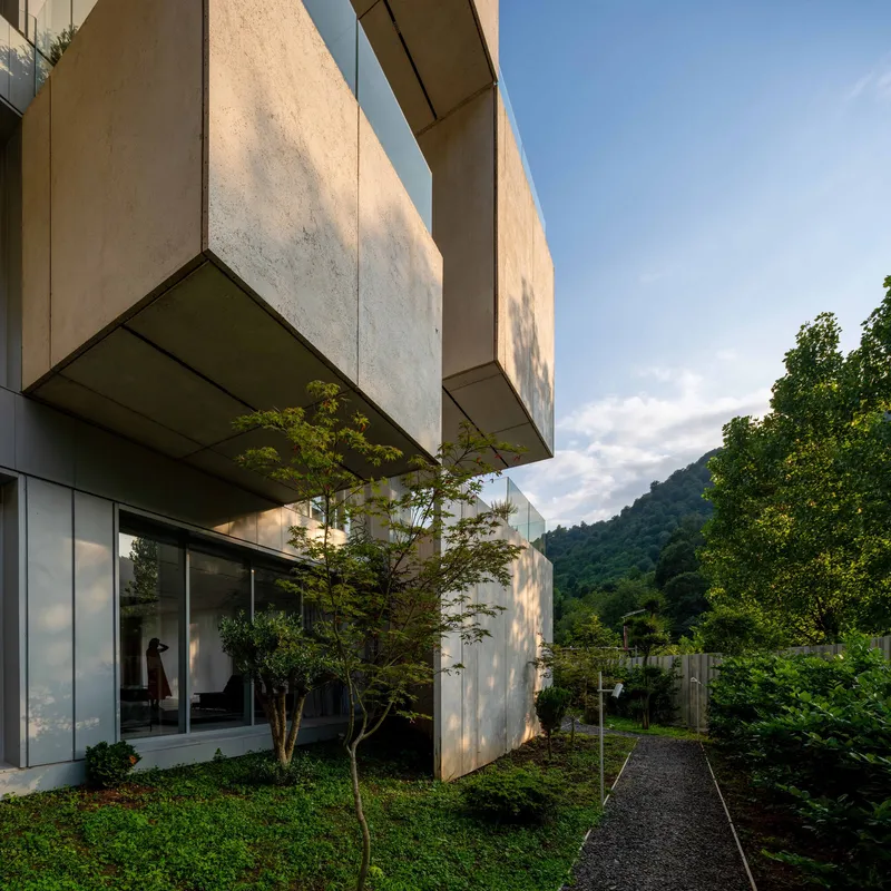 Side view of stacked concrete volumes with trees between levels and hillside in the background