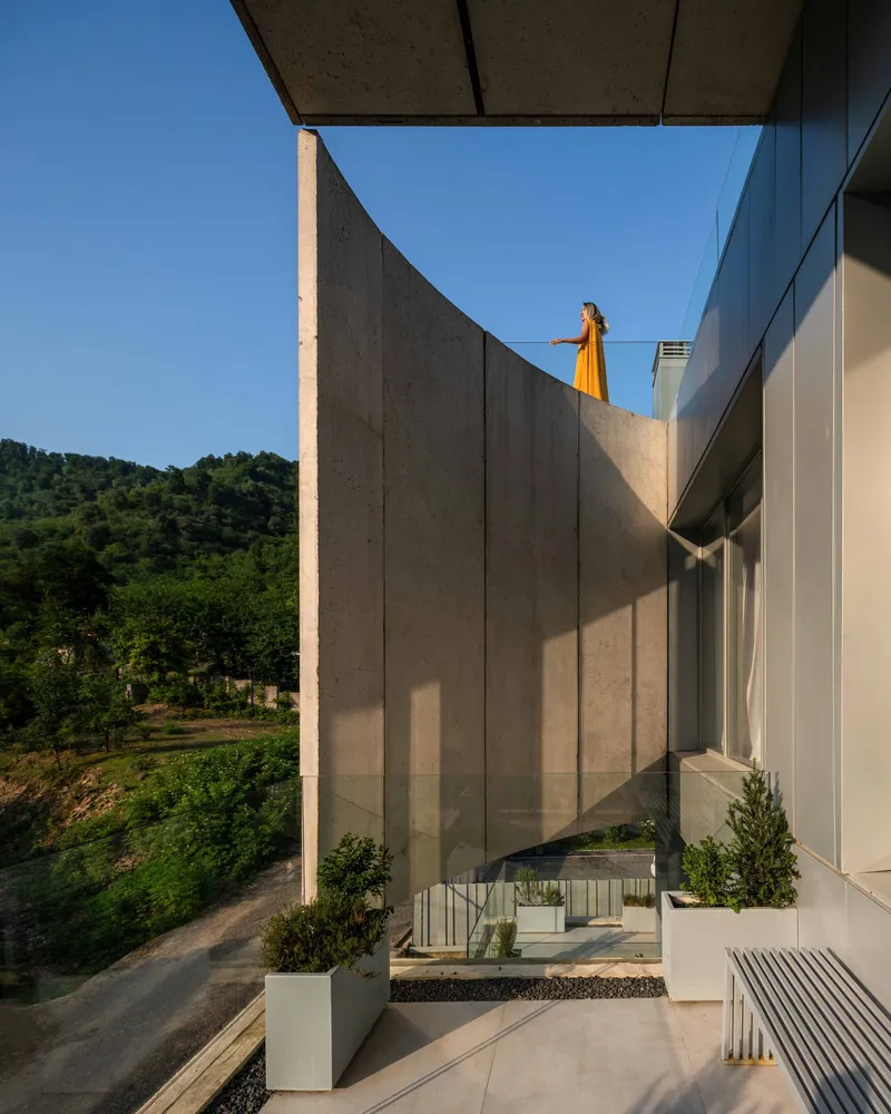 Upper terrace with curved concrete wall and planted beds overlooking forested hills at dusk