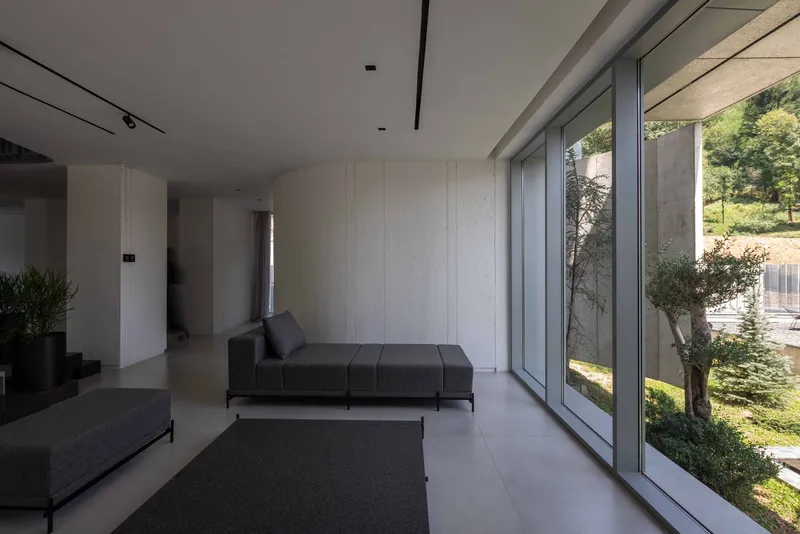 Interior living space with full-height glazing and pale paneled wall opening to terrace and garden