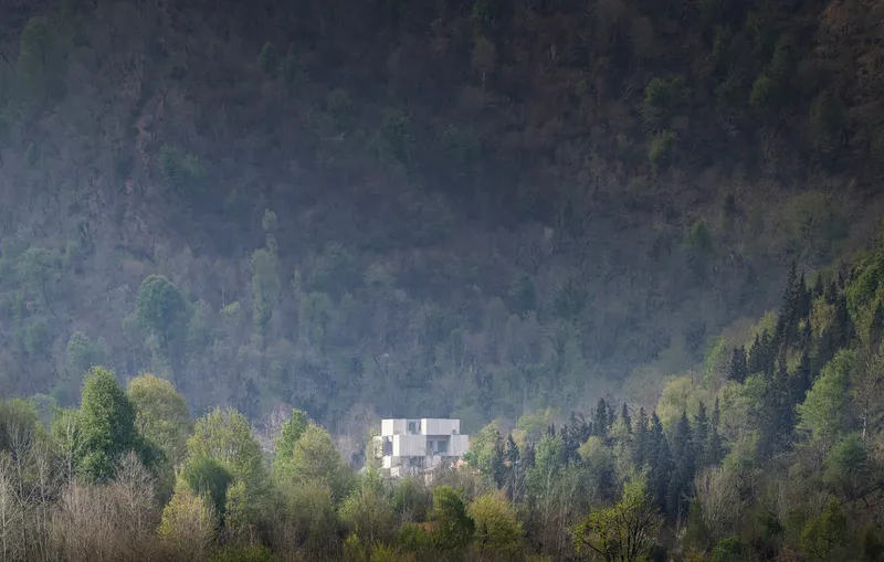 White geometric volumes nestled among deciduous and evergreen forest in morning mist
