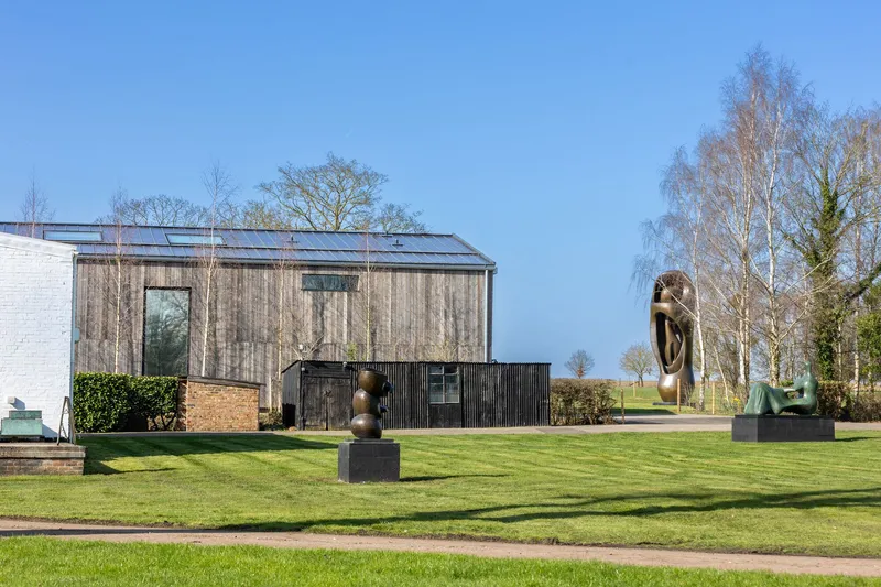 Timber and brick volumes beside a manicured lawn with bronze sculptures and birch trees