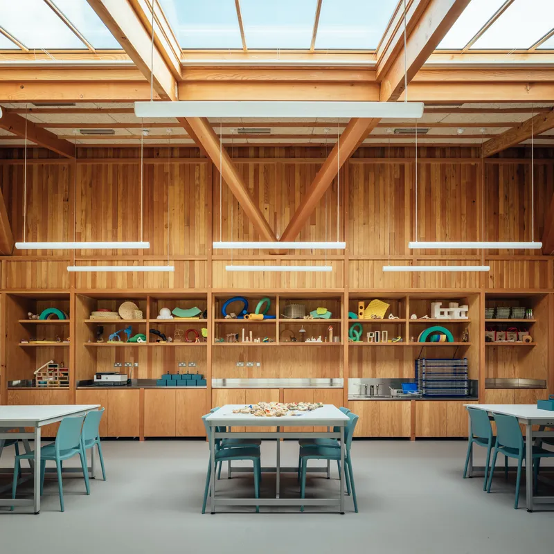Storage wall with timber shelving beneath exposed beams and continuous roof glazing with suspended light fixtures