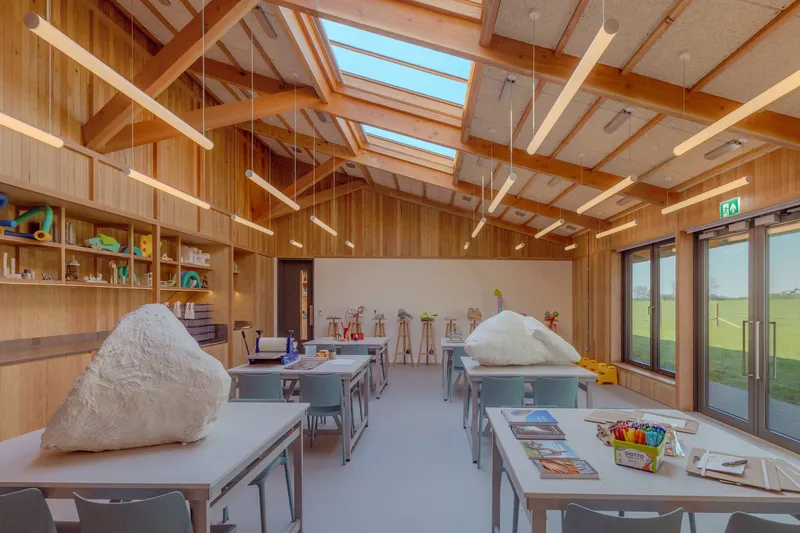 Classroom interior with exposed timber beams, skylights and pendant lights illuminating white work tables