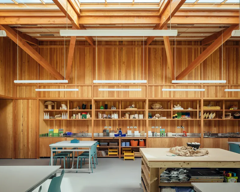 Vertical timber wall with built-in shelving displaying student work beneath suspended linear lighting fixtures