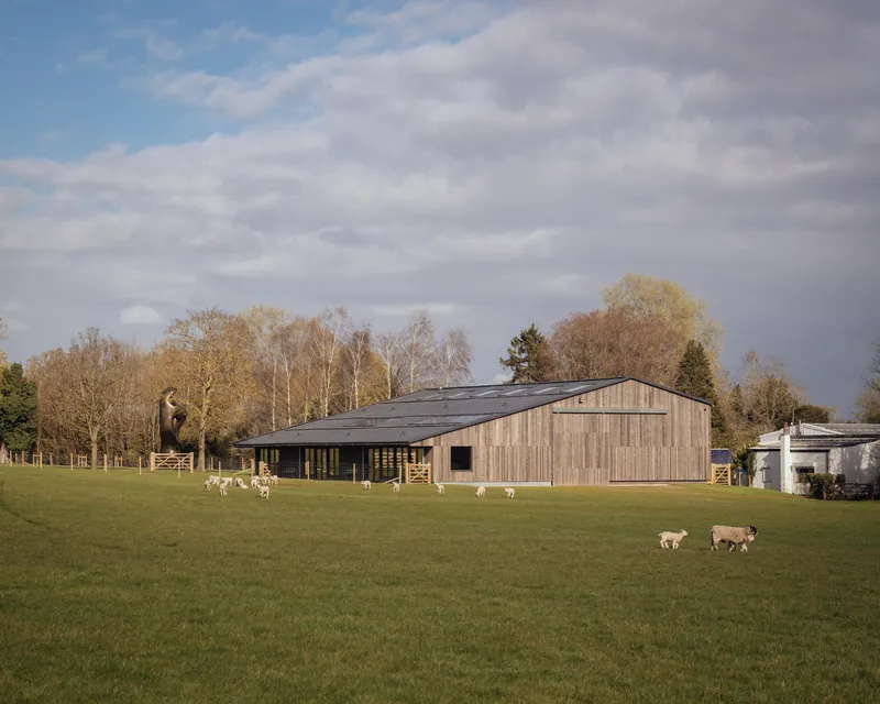 Timber-clad gabled building in a green field with grazing sheep and bare winter trees