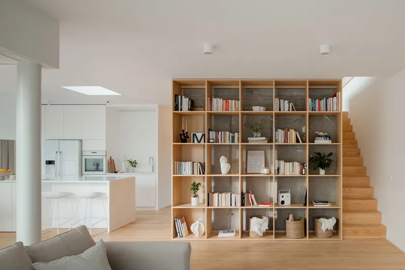 Tall gridded timber shelving unit separating living space from timber staircase and kitchen beyond