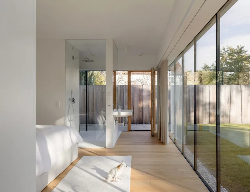 Bedroom with glazed walls opening to courtyard and glass-enclosed shower in morning sunlight