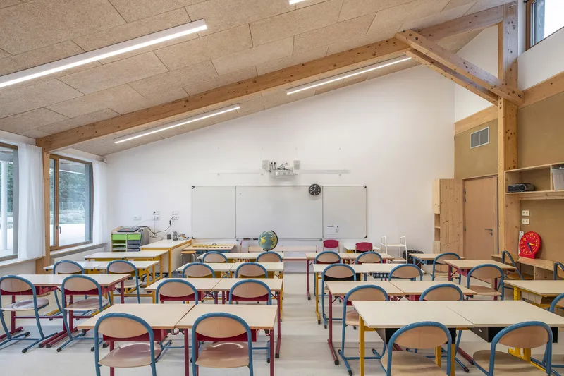 Classroom with rows of tables and chairs facing a whiteboard under exposed timber beams and ceiling panels