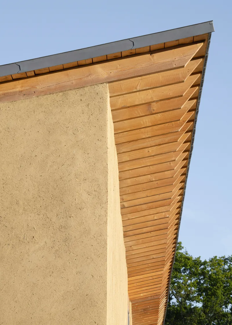 Corner detail of the sloped timber eave meeting a rammed earth wall under blue sky