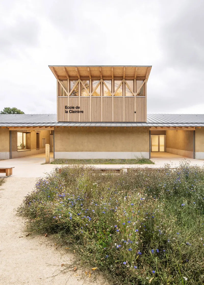 Timber tower with diagonal bracing above earthen base wall facing courtyard with wildflower planting