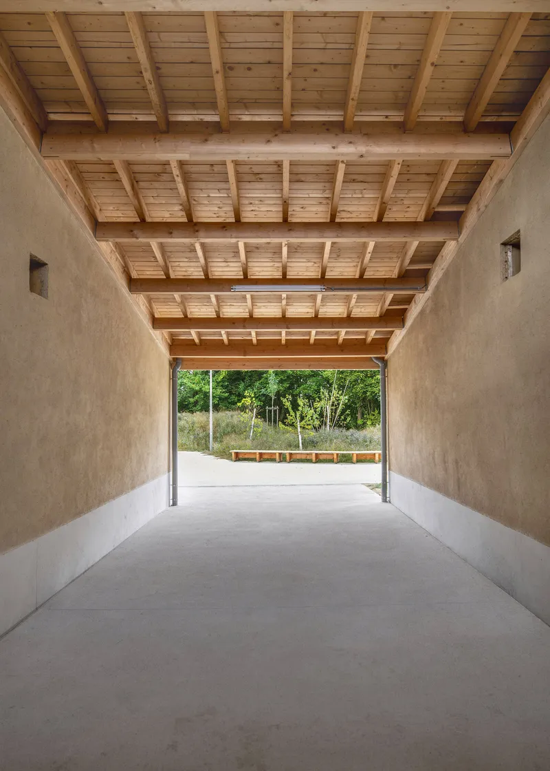 Covered passage with exposed timber joists and beams over polished concrete leading to a garden