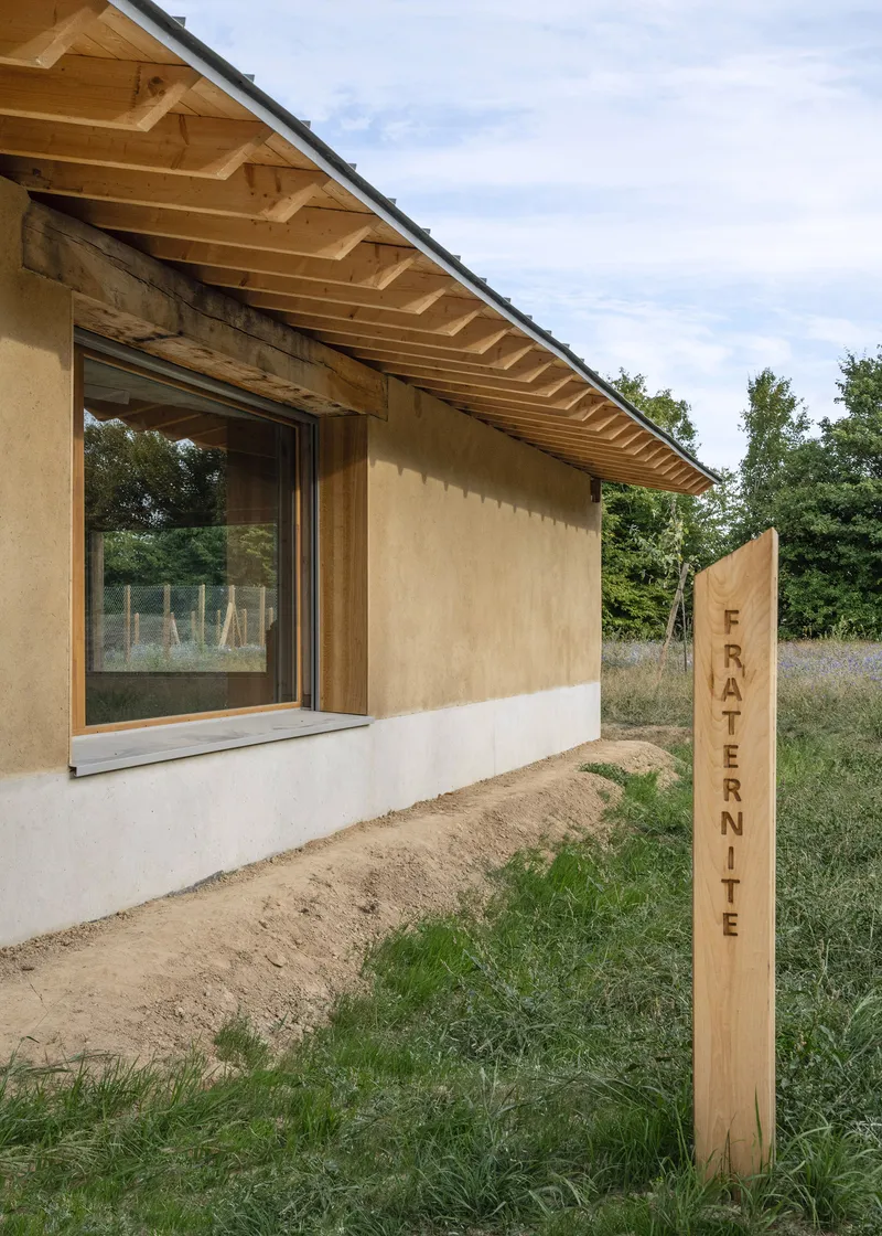 Corner detail showing plywood wall with exposed timber rafters above a white plaster base and timber signpost