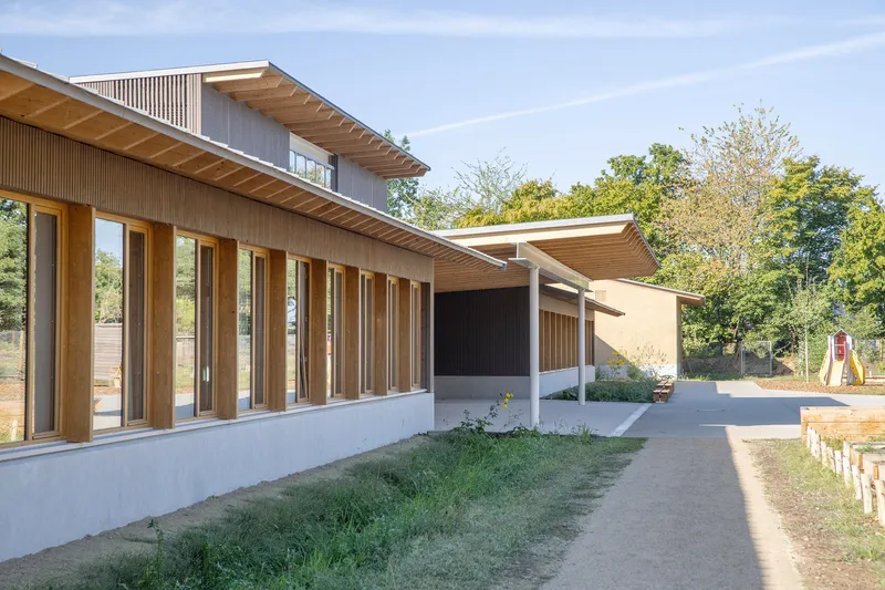 Long view of linked volumes with deep timber eaves and vertical fin facades amid autumn trees