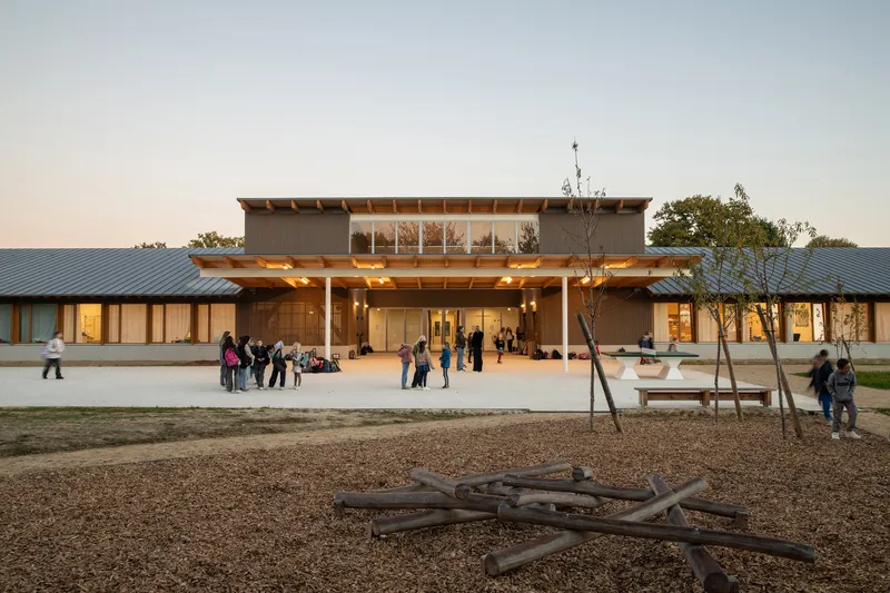 Evening view of the central two-story volume with glazed upper floor and people gathering at dusk