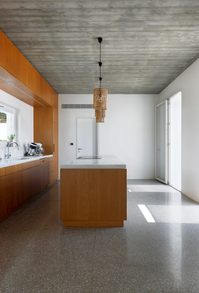 Kitchen with timber island and terrazzo flooring under a horizontal board-formed concrete ceiling