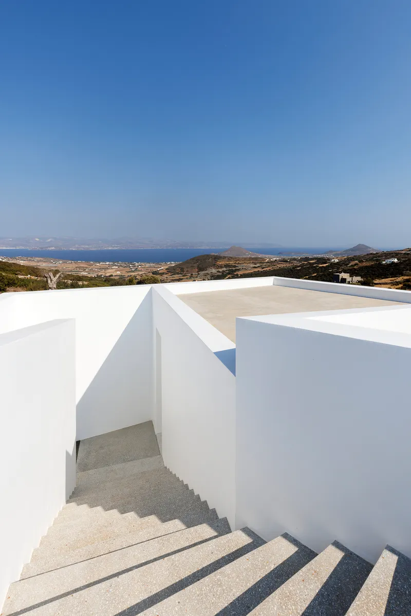 Terrazzo staircase descending between white rendered walls with a coastal landscape beyond