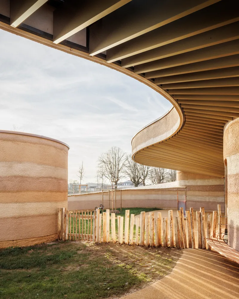 Covered outdoor space with timber slatted soffit wrapping around rammed earth walls and wooden fencing in winter light
