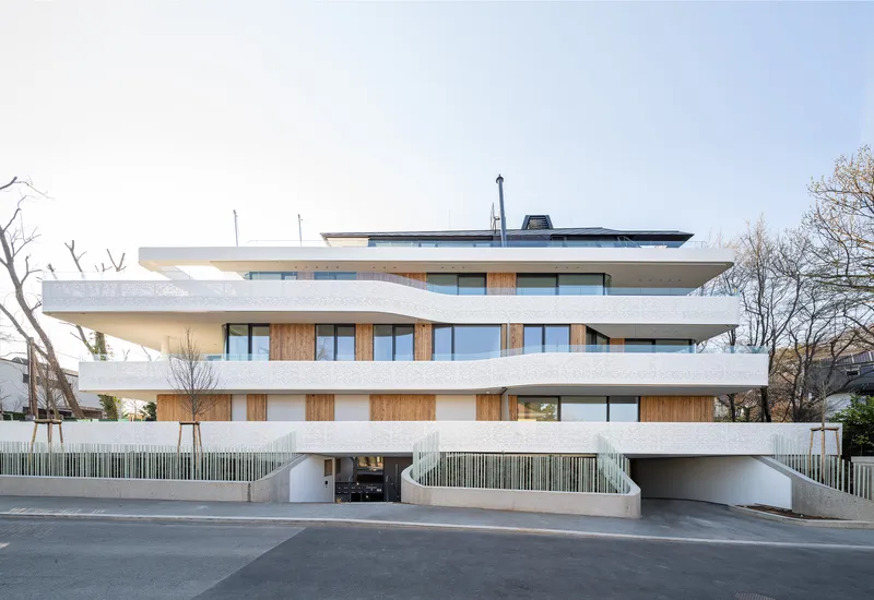 Street view of the layered concrete balconies and timber cladding with bare winter trees overhead