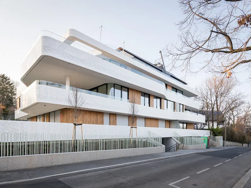 Side facade showing stacked terraces with perforated metal railings and concrete base wall from the roadway