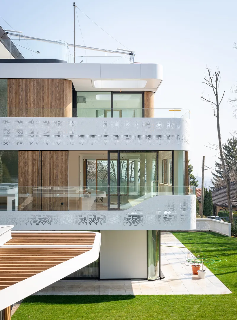 Garden facade revealing three levels of timber-clad volumes with perforated balcony screens and a lawn below