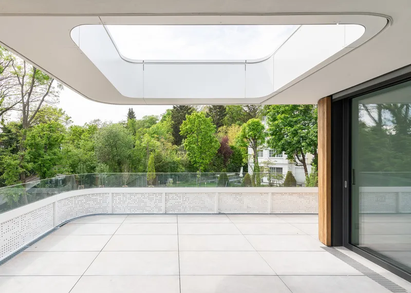 Curved terrace with perforated metal balustrade and recessed skylight opening framing green tree canopy beyond