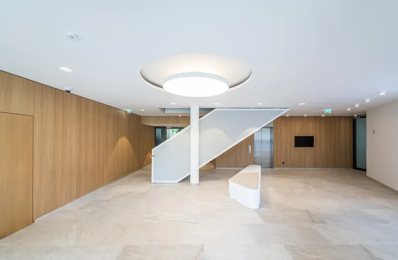 Entrance lobby with curved white staircase wrapping a circular column against timber-paneled walls