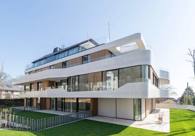 Corner view of the wraparound facade with perforated concrete balconies and timber panels above the lawn