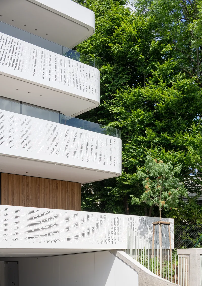 Close-up of curved balconies with perforated white railings against dense green tree canopy