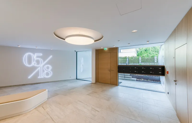Entrance lobby with circular pendant light, timber door, and neon numerals on white wall