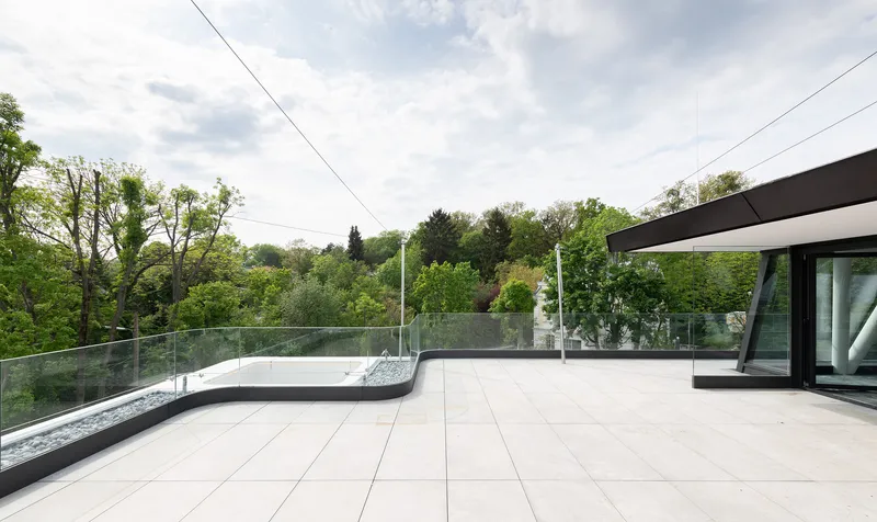 Rooftop terrace with pale pavers, glass balustrade, and tree canopy under cloudy sky