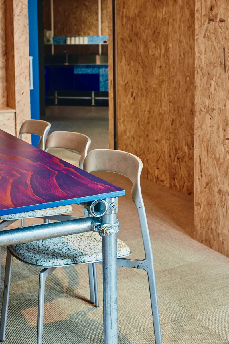 Marbled resin tabletop with scaffolding legs and white chairs against oriented strand board walls