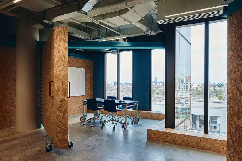Meeting space enclosed by oriented strand board partitions on castors with floor-to-ceiling glazing beyond