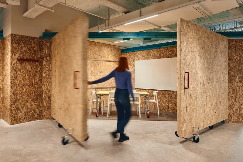 Person walking past reconfigurable oriented strand board partitions with concrete columns wrapped in natural fiber