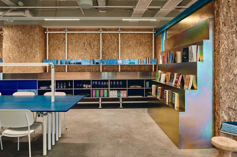 Interior workspace with oriented strand board walls, iridescent metal shelving, and exposed mechanical ceiling systems